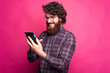© Vulp - A bearded man is holding a tablet and smiling at it near pink wall