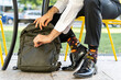 © VITTA GALLERY/Westend61 - Male entrepreneur wearing colorful socks zipping backpack while sitting on chair at sidewalk cafe