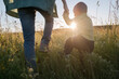 © Ekaterina Yakunina/Westend61 - Cute boy holding mother's hand while walking on field during sunny day