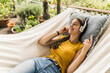 © UWE_UMSTAETTER/Westend61 - Woman with eyes closed listening music through headphones while relaxing on hammock in yard