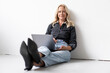 © Robijn Page/Westend61 - Smiling businesswoman using laptop while sitting on floor against wall in office