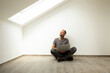 © MiJo/Westend61 - Mature man with laptop looking through window while sitting against white wall in attic of new house