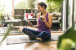 © UWE_UMSTAETTER/Westend61 - Smiling young woman holding drink while using digital tablet on exercise mat at home