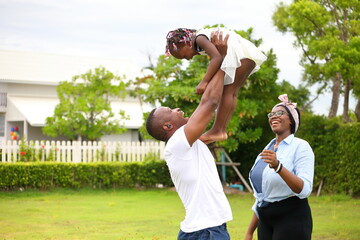 African American family playing with young happy little daughter on green grass field while enjoying summer garden outside the house in the neighborhood with copy space