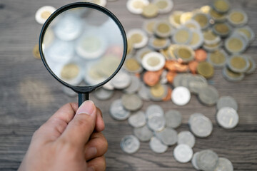 Coins with magnifier glass on wooden background. Saving and investment concept.