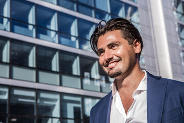 Young business man smiling and happy outdoors with a modern building behind. The man is wearing a white shirt and a smart jacket.