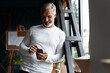 © opolja - Casual Grey-haired Mature businessman using smartphone standing by the window