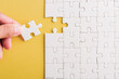© sorapop - Top view flat lay of hand-holding last piece white paper jigsaw puzzle game last pieces put to place for solve problem complete mission, studio shot on a yellow background, quiz calculation concept