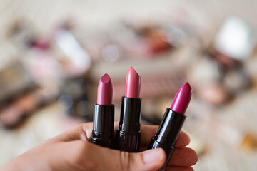 Female hand holding three lipsticks pink color