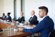 © AnnaStills - Mature businessman sitting at the table using microphone to speak a speech for business people during conference