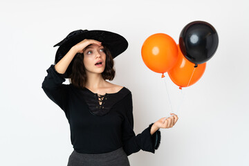 Young witch holding black and orange air balloons doing surprise gesture while looking to the side