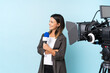 © luismolinero - Reporter woman holding a microphone and reporting news over isolated blue background looking to the side