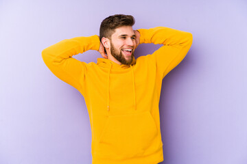 Wall Mural - Young man isolated on purple background feeling confident, with hands behind the head.