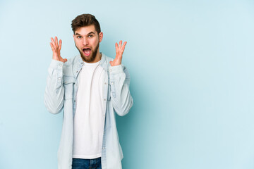 Wall Mural - Young caucasian man isolated on blue background celebrating a victory or success, he is surprised and shocked.