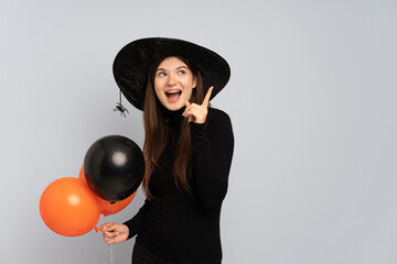 Young witch holding black and orange air balloons intending to realizes the solution while lifting a finger up