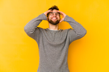 Wall Mural - Young caucasian man isolated on yellow background laughs joyfully keeping hands on head. Happiness concept.