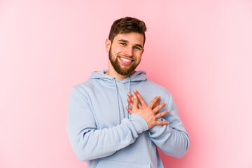 Wall Mural - Young caucasian man isolated on pink background has friendly expression, pressing palm to chest. Love concept.