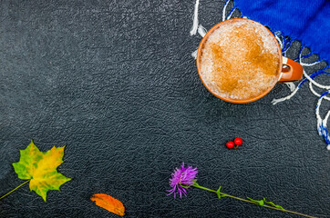 Wall Mural - Cup of coffee cappuccino with cinnamon, blue stole, autumn leaves, Rowan berries, flower on a black background with copy space, top view, flat lay. Beautiful autumn composition, beautiful background.