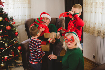 Senior couple and two children are spending time together in the living room. They are opening Christmas presents.