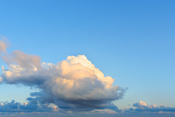 Wall Mural - large fluffy cumulus cloud tinted golden color by the evening sun. pale orange cloud against bright 