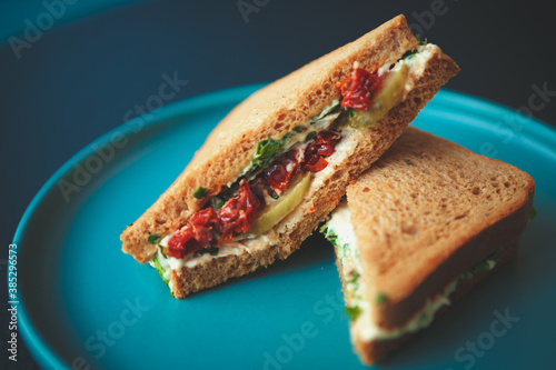 Healthy fast food for lunch.Club sandwich with natural ingredients:dry tomato,pickled cucumbers,wholegrain toast bread served on blue plate in vegan restaurant for breakfast.Delicious snack fastfood