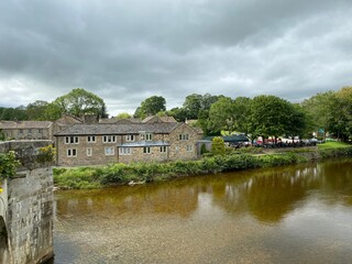 Wall Mural - Looking from the stone bridge, over the River Wharfe, with housing, trees, and heavy rain clouds in, Burnsall, Skipton, UK