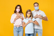 © ViDi Studio - Young parents mom dad with child kid daughter teen girl in t-shirts face mask to safe from coronavirus virus covid-19 holding hands folded on hearts isolated on yellow background. Family day concept.