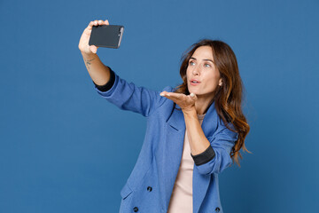 Wall Mural - Pretty charming beautiful young brunette woman 20s wearing basic jacket doing selfie shot on mobile phone blowing sending air kiss isolated on bright blue colour wall background, studio portrait.