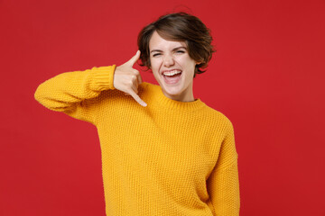 Cheerful funny attractive young brunette woman 20s wearing basic casual yellow sweater standing doing phone gesture like says call me back isolated on bright red colour background studio portrait.