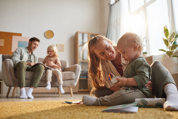 happy mother playing with her baby on the floor and father playing with older son in the background 