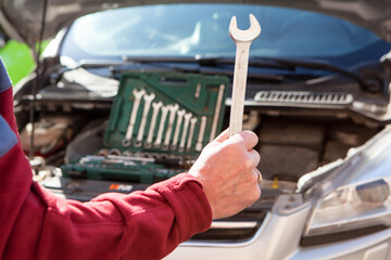 Male arm holding steel wrench for car repair. Vehicle engine is on background