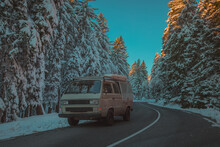 Front View Of An Adventure Vintage Retro Campervan Or Off Road Vehicle On A Snowy Road During Colorful Sunset Or Sunrise. Adventourous Journey In Winter Forest With Campervan.