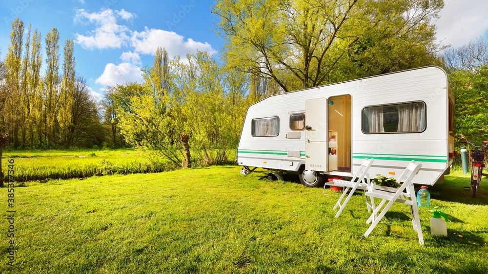 Caravan trailer on a green lawn, on a sunny spring day. Transportation, vacations, weekend, road trip, home, alternative lifestyle, leisure activity, camping - obrazy, fototapety, plakaty 