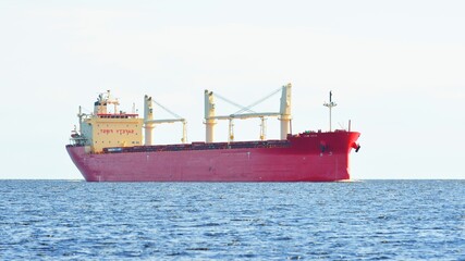 Large red cargo ship (bulk carrier) sailing near Vlissingen, the Netherlands. Panoramic view. Freight transportation, fuel, power generation, logistics, industry, global communications, environment