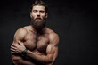 © Fxquadro - Naked man with muscular build and beard posing with crossed arms looking at camera in dark background.