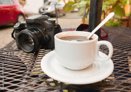Cuadros en Lienzo una taza de café como primer plano al exterior de una cafetería y una cámara en segundo plano