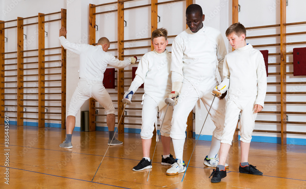 Coach demonstrating to teenage athletes stances and movements with rapier during fencing workout - obrazy, fototapety, plakaty 