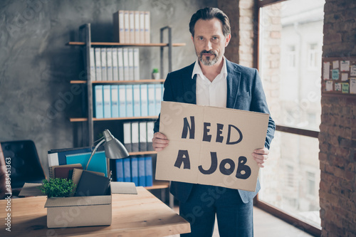 Portrait of his he serious jobless guy realtor economist holding in hands placard saying need a job find solution at modern loft industrial brick style interior workplace workstation