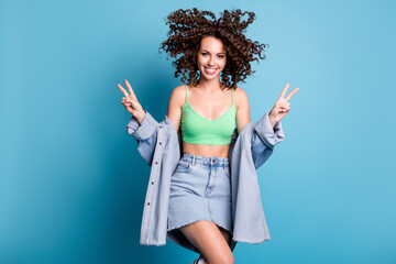 Sticker - Photo of cute charming student lady smiling raise hands show v-sign welcoming friends party wear green crop top naked abdomen denim jacket mini skirt isolated blue color background