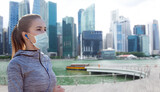 Fototapeta Tematy - fitness, sport and health concept - woman wearing face protective medical mask for protection from virus disease running and listening to music in earphones over singapore city marina background