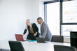 © Mangostar - Couple of business colleagues or partners starting meeting in conference room, standing at table and using laptop together. Wide shot. Business communication concept