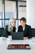 © Mangostar - Focused excited businesswomen looking at laptop display while sitting at table with cups of coffee in office. Front view. Teamwork and communication concept