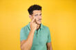 © Irene - Young handsome man wearing green casual t-shirt over isolated yellow background Pointing to the eye watching you gesture, suspicious expression