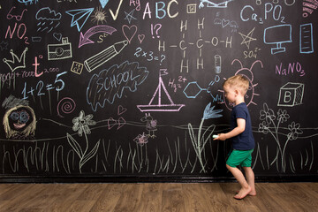 a little three-year-old boy runs near a slate wall and draws with multi-colored chalk. European appearance. training in drawing.