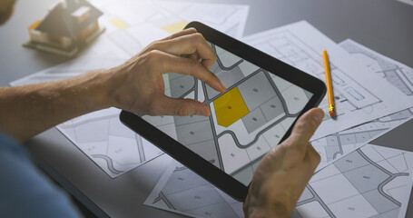 Wall Mural - man searching building plot to buy on cadastral plan for house construction on digital tablet