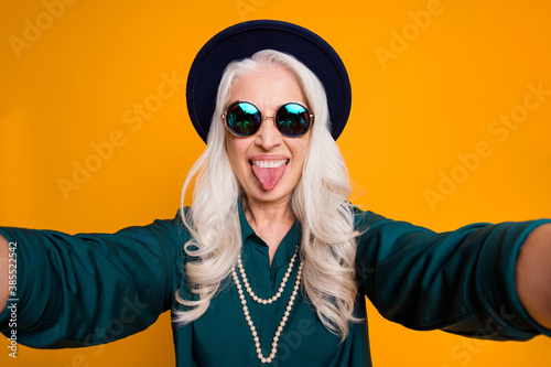 Closeup photo of cool crazy white haired granny lady make selfies feel young stick tongue out mouth wear green shirt sun specs luxury necklace isolated yellow bright color background
