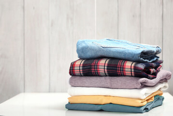 Wall Mural - Stack of clothing on white table wooden plank background.Folded clothes pile empty copy space.