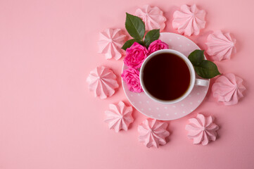 A cup of tea on a delicate pink background with pink meringues.