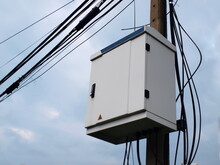 Internet Control Cabinet On A Pole. NODE Is A Box That Combines The Cables Of High Speed Internet On The Sky Background There Are White Clouds. Selective Focus