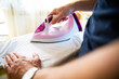 Man ironing clothes on an ironing board using a steam iron, close-up and focus on an iron and a hand.